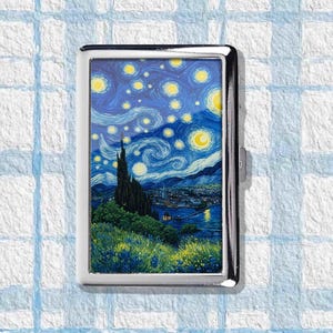May include: A silver metal cigarette case featuring a print of Van Gogh's "Starry Night" painting. The case has a rectangular shape with rounded corners and a clasp closure. The artwork depicts a night sky with swirling clouds, stars, and a village.