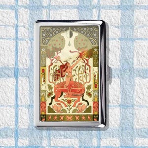 May include: A silver cigarette case with a vibrant, artistic design. The artwork depicts a nude figure riding a mythical creature, with trees, flowers, and other decorative elements. The case is rectangular and has a hinged lid.