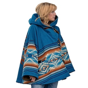 May include: A hooded blue poncho with a Southwestern-inspired pattern in shades of brown, orange, and cream. The poncho features a toggle closure and a cozy, warm design, perfect for cooler weather. The garment is made of a thick, woven material.
