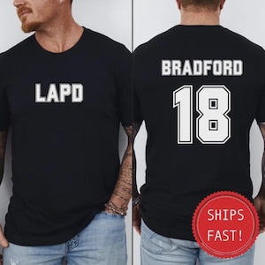 May include: Black t-shirt with the text "LAPD" in white block letters on the front. The back of the shirt displays "BRADFORD" above the number "18" in white block letters. The shirt has a crew neck.