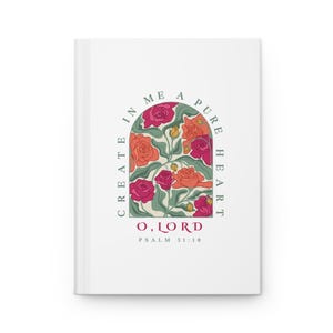 May include: A white hardback journal featuring an arched illustration of red, orange, and pink roses with green leaves. The text reads "CREATE IN ME A PURE HEART O, LORD PSALM 51:10" in a mix of dark grey and red lettering centred on the front cover.