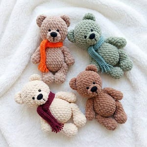 May include: Four handmade crochet teddy bears in tan, green, cream, and brown. Each bear has a black nose and wears a scarf in orange, blue, burgundy, and brown. The bears are on a white, textured surface.