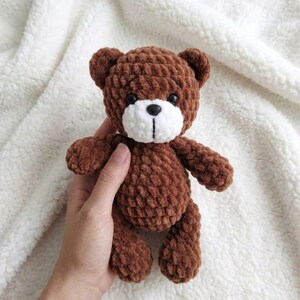 May include: A handmade brown teddy bear with a white muzzle and black eyes. The bear is made of a textured, plush material and has a classic teddy bear shape. The bear is a soft toy.