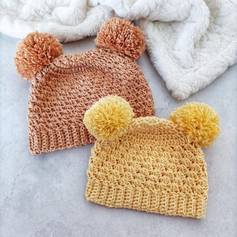Puede incluir: Dos gorros de ganchillo con un patr&oacute;n de punto de estrella texturizado y bordes acanalados. Un gorro es de color beige c&aacute;lido con dos pompones a juego, y el otro es de color amarillo brillante con dos pompones amarillos a juego arriba.