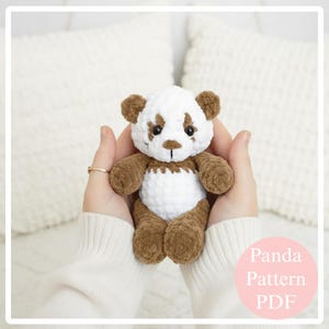 May include: A handmade crochet panda bear with a white body, brown accents, and black eyes. The panda is held in two hands. The text "Panda Pattern PDF" is in a pink circle in the lower right corner.