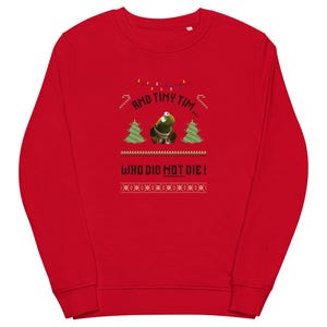 Puede incluir: Una sudadera roja con un gráfico que presenta un personaje verde, árboles de Navidad y el texto "AND TINY TIM... WHO DID NOT DIE!". El diseño incluye luces de cadena y un patrón festivo.