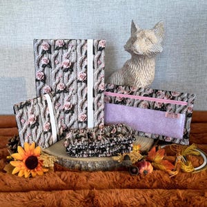 May include: A selection of floral-patterned accessories, including a journal, pencil case, and scrunchie. The items display a rose design on a cable knit texture. A fox ornament and autumn leaves are also present.