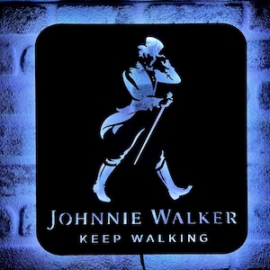 Puede incluir: Letrero cuadrado negro con esquinas redondeadas, con el logotipo de Johnnie Walker en blanco. El logotipo representa a un hombre caminando con un bastón. Las palabras "Johnnie Walker" y "Keep Walking" están debajo. El letrero está iluminado con un brillo azul.