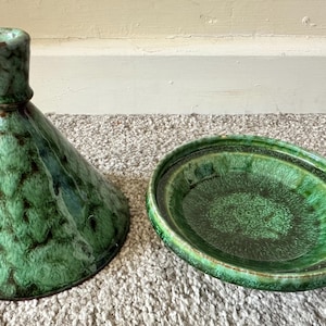 May include: A green ceramic candle holder and a matching dish. The candle holder is cone-shaped with a flared base and a narrow top. The dish is oval with a raised rim. Both pieces have a mottled green glaze.