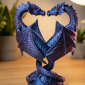 May include: A detailed sculpture of two dragons facing each other, forming a heart shape with their bodies. The dragons are a deep blue with iridescent highlights, and their wings are spread. The sculpture sits on a decorative base, showcasing a fantasy theme.