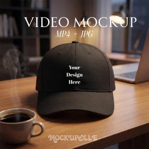 May include: A black baseball cap with the text "Your Design Here" in white. The cap is on a wooden surface, with a coffee cup and a laptop in the background. The image also includes the text "VIDEO MOCKUP MP4 + JPG".