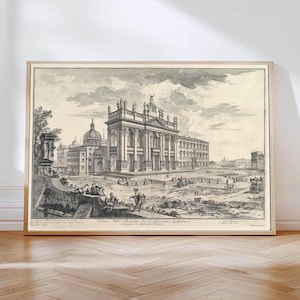 Op de afbeelding: Ingelijste zwart-wit architectuurprint met een gedetailleerd stadsbeeld met een groot gebouw met zuilen en beelden. De print bevat tekst aan de onderkant en wordt weergegeven in een lichtgekleurde houten lijst.