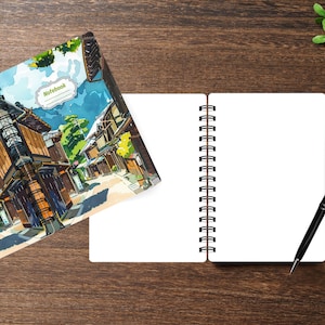 May include: A spiral-bound notebook featuring a colorful illustration of a traditional street scene with wooden buildings and a blue sky on the cover, alongside an open notebook with blank white pages and a black ballpoint pen resting nearby.