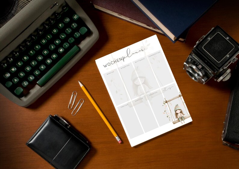 May include: A weekly planner with the German text "Wochenplaner" is displayed on a wooden desk. The planner features illustrations of a girl on a swing and other decorative elements. A vintage typewriter, pencil, and camera are also on the desk.