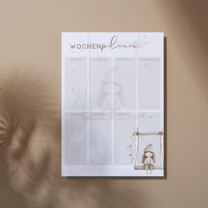 May include: A weekly planner with the German text "Wochenplaner" at the top. The planner features a watercolor illustration of a girl on a swing. The design includes soft colors and floral accents, creating a gentle and inviting aesthetic.