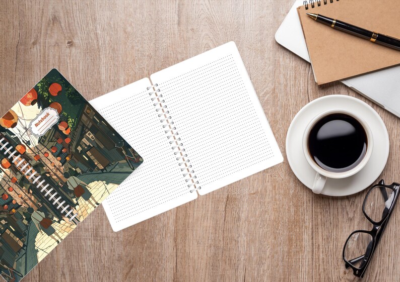 May include: An open spiral notebook with dotted pages sits next to a closed notebook with a colorful illustration. A cup of coffee, glasses, a pen, and a laptop are on a wooden surface. The closed notebook has the word "Notebook" on it.