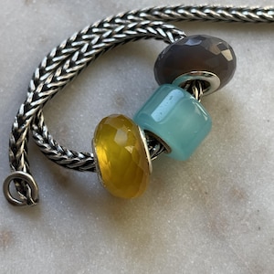 Op de afbeelding: Een set van drie keramische mokken met een gespikkelde, matte afwerking. De mokken zijn in cr&egrave;me, lichtgrijs en donkergrijs. Elke mok heeft een eenvoudig, minimalistisch ontwerp en een afgeronde handgreep.