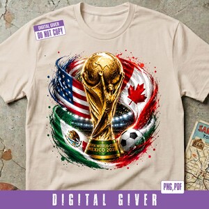 May include: A beige t-shirt featuring a graphic of the FIFA World Cup trophy centered between the flags of the United States, Canada, and Mexico. The design includes a soccer ball, stadium lights, and the text FIFA WORLD CUP MEXICO 2026.