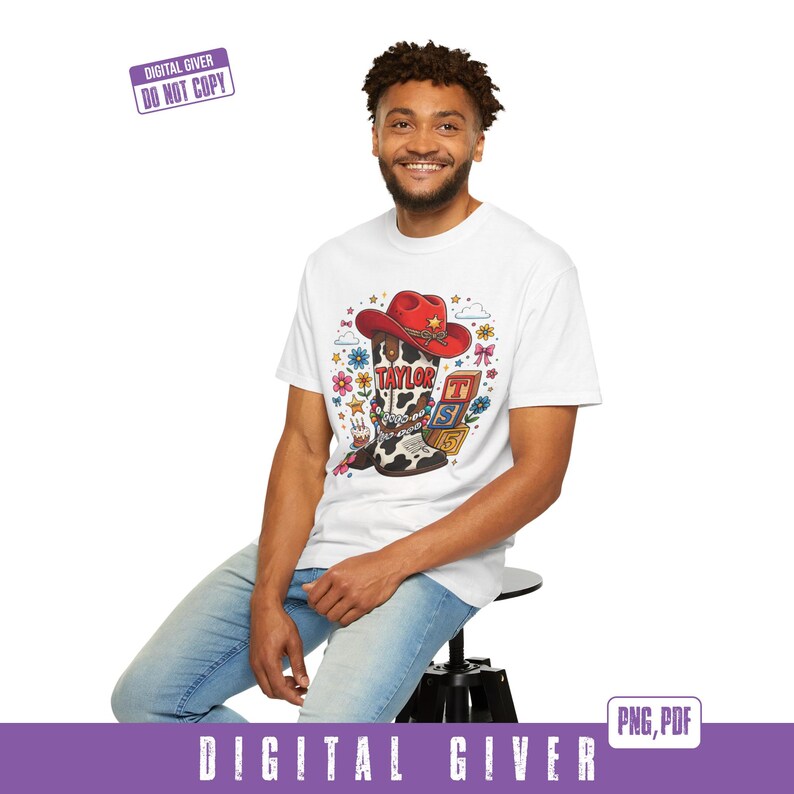 May include: A white t-shirt featuring a graphic print of a cow-print cowboy boot topped with a red cowboy hat. The boot is decorated with beads and the name TAYLOR. Nearby are colorful alphabet blocks, flowers, stars, and a small birthday cake.