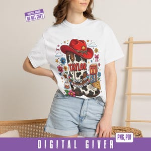 May include: A white t-shirt featuring a graphic of a red cowboy hat atop a cow-print boot. The boot displays the text TAYLOR and I KNEW IT I KNEW YOU on a beaded string. Surrounding elements include colorful flowers, stars, and alphabet blocks.