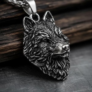 May include: A silver-colored wolf head pendant on a chain. The pendant features detailed fur texture and a realistic wolf face. The chain is a braided style. The pendant is likely made of stainless steel or a similar metal.