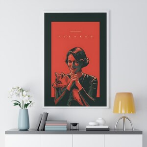 May include: A framed art print featuring a woman holding a fox against a red background. The word "FLEABAG" is printed at the top. The artwork is in a white frame and is displayed on a white wall.