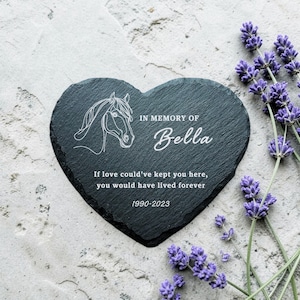 May include: A heart-shaped black slate memorial stone with a horse head outline and the text "IN MEMORY OF Bella". The inscription reads "If love could've kept you here, you would have lived forever 1990-2023". Lavender sprigs are in the background.