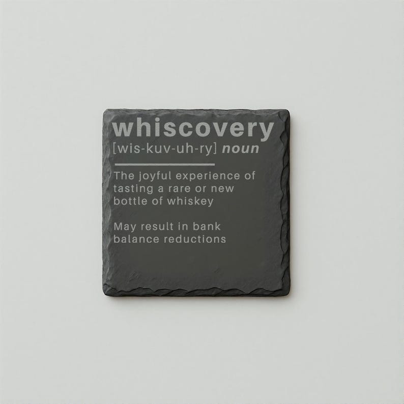 Puede incluir: Un posavasos cuadrado de pizarra gris oscuro con la palabra "whiscovery" en texto blanco. La definici&oacute;n de "whiscovery" est&aacute; impresa debajo, describiendo la experiencia de degustar whisky raro. El texto inferior advierte sobre posibles reducciones del saldo bancario.