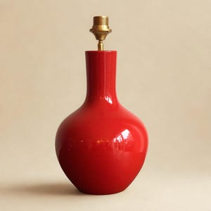 Peut inclure: Un pied de lampe en c&eacute;ramique rouge brillant avec une douille en laiton. La lampe a un corps arrondi et un col &eacute;troit. La lampe est d'un rouge vif et a une surface lisse et r&eacute;fl&eacute;chissante. Un luminaire d&eacute;coratif.