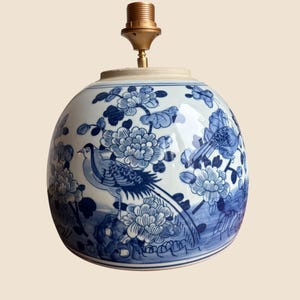 Pode incluir: Base de lâmpada redonda em cerâmica com um design floral e de pássaros em azul e branco. A lâmpada tem um suporte de lâmpada de latão. O design apresenta ilustrações detalhadas de flores e pássaros, criando um visual clássico e decorativo.