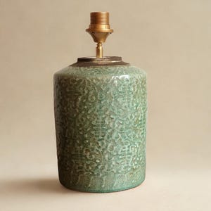 May include: A green ceramic lamp base with a textured, crackled pattern. It has a brass-coloured socket and a dark metal ring. The lamp base is cylindrical in shape. This decorative item is suitable for home decor.