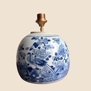 Puede incluir: Base de lámpara redonda de cerámica azul y blanca con un portalámparas de latón. La base de la lámpara presenta un diseño floral y de pájaros en tonos azules. La base de la lámpara tiene forma bulbosa y un acabado liso y brillante.