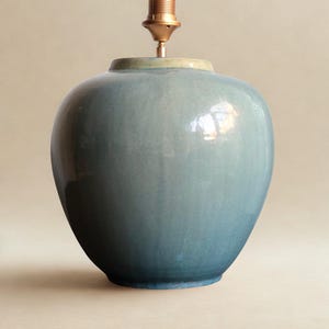 Könnte beinhalten: Ein blauer Keramik-Lampenfuß mit einer Messing-Lampenfassung. Die Lampe hat eine abgerundete, vasenartige Form mit einem Farbverlauf von Blautönen. Der obere Rand ist hellgrün.