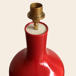 Peut inclure: Un pied de lampe de table en c&eacute;ramique rouge avec un support de lampe en laiton. Le pied de lampe a une forme arrondie et une finition brillante. La lampe est con&ccedil;ue pour contenir une ampoule et un abat-jour. La lampe est un objet d&eacute;coratif.