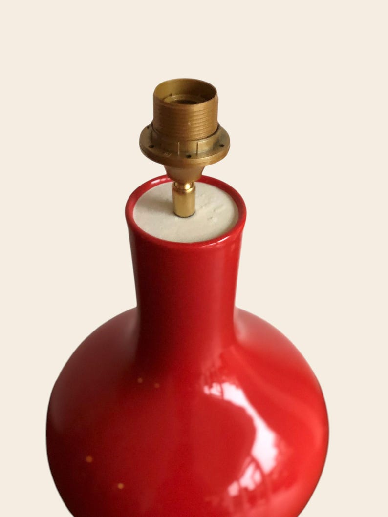 Peut inclure: Un pied de lampe de table en c&eacute;ramique rouge avec un support de lampe en laiton. Le pied de lampe a une forme arrondie et une finition brillante. La lampe est con&ccedil;ue pour contenir une ampoule et un abat-jour. La lampe est un objet d&eacute;coratif.
