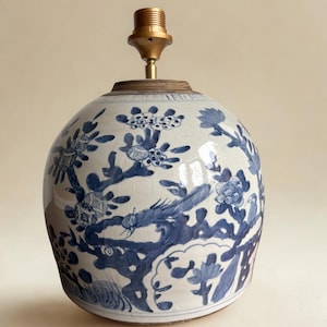 Könnte beinhalten: Runder Keramik-Lampenfuß mit blau-weißem Blumenmuster. Die Lampe hat oben einen messingfarbenen Lampenhalter. Das Design zeigt stilisierte Blumen und Zweige. Ein dekorativer Einrichtungsgegenstand.
