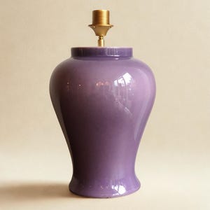 May include: A glossy, purple ceramic lamp base with a brass lamp holder. The lamp base has a rounded top and a flared base. The lamp is designed to hold a lampshade. The overall shape is reminiscent of a vase.