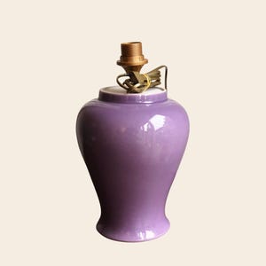 May include: A glossy, purple ceramic lamp base with a brass lamp holder. The lamp base has a rounded body that tapers towards the base. The lamp base is a solid color and has a smooth, reflective surface. The lamp base is designed to hold a lampshade.