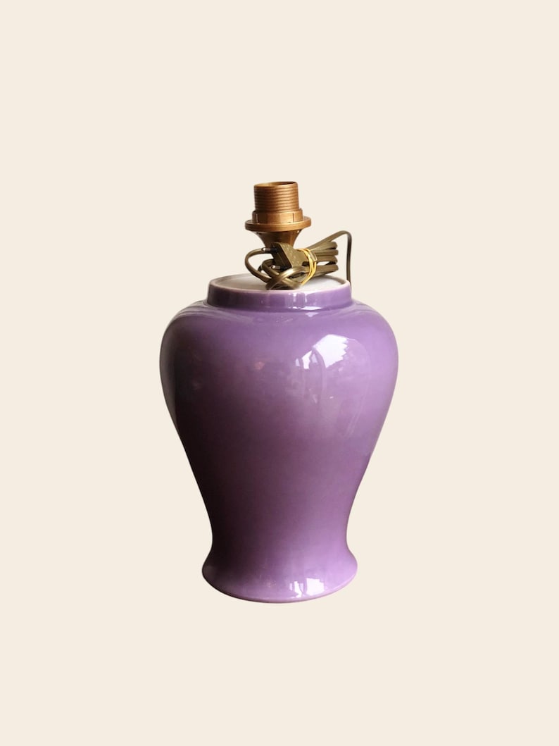 May include: A glossy, purple ceramic lamp base with a brass lamp holder. The lamp base has a rounded body that tapers towards the base. The lamp base is a solid color and has a smooth, reflective surface. The lamp base is designed to hold a lampshade.