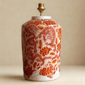 Peut inclure: Un pied de lampe cylindrique en céramique avec un motif de dragon et de fleurs rouges sur fond blanc. Le luminaire est surmonté d'un support de lampe en laiton. Style asiatique traditionnel.