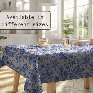 May include: A rectangular tablecloth with a blue floral pattern on a white background. The tablecloth is draped over a wooden table. The text "Available in different sizes" is displayed in a white rectangle.