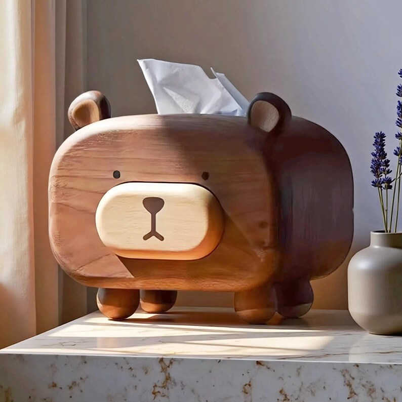 May include: A wooden bear-shaped tissue box dispenser. The bear is brown with a lighter brown snout and small black eyes. White tissues are visible coming out of the top. The dispenser sits on a marble surface.