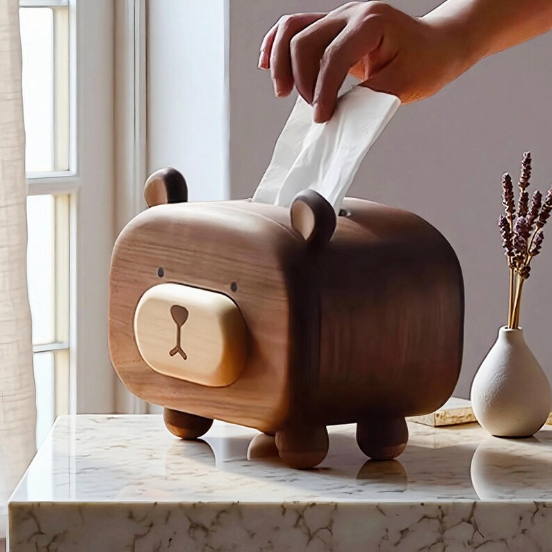 May include: A wooden bear-shaped tissue box with a light brown face and dark brown body. The bear has small ears and a nose. White tissues are being pulled from the top opening. The tissue box is on a marble surface.