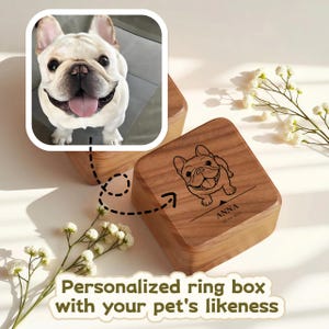 May include: Wooden ring box with a French Bulldog illustration and the name "ANNA" and a date. The box is square and has a hinged lid. The image also includes a photo of a French Bulldog and the text "Personalized ring box with your pet's likeness."