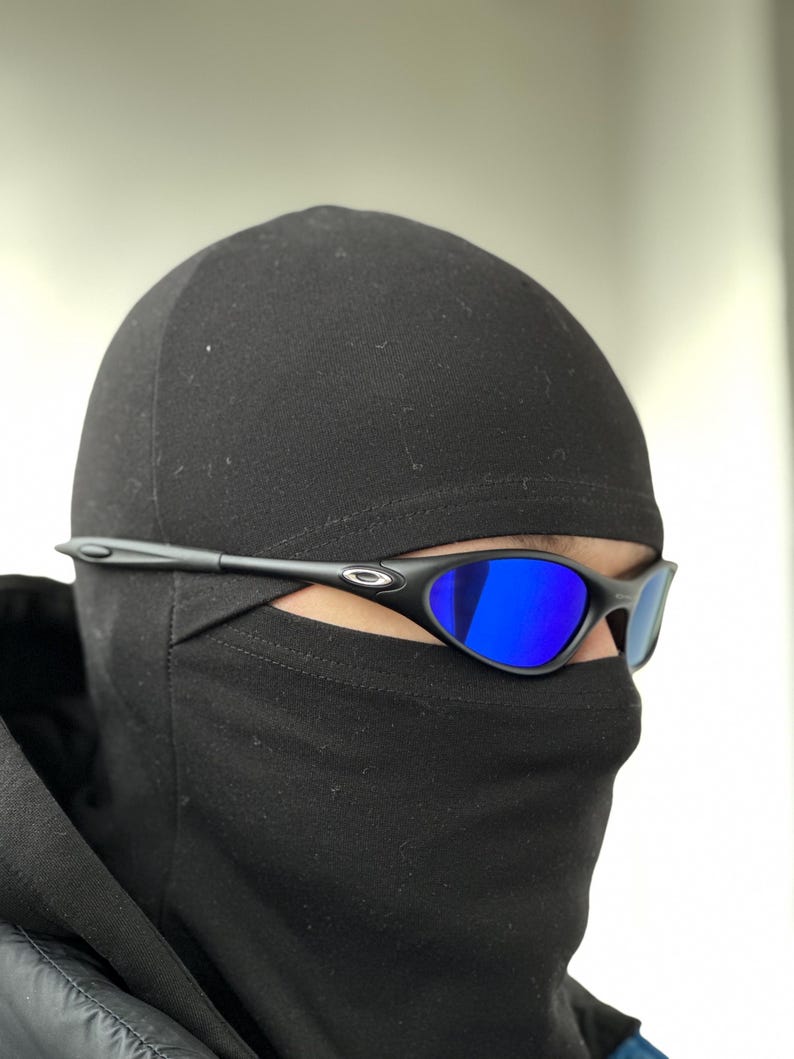 K&ouml;nnte beinhalten: Schwarze Sonnenbrille mit blau verspiegelten Gl&auml;sern. Die Sonnenbrille hat ein schlankes, modernes Design mit einem schwarzen Rahmen. Das Bild zeigt die Sonnenbrille in Kombination mit einer schwarzen Sturmhaube.