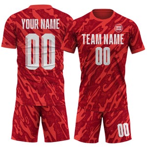 May include: Red athletic uniform set with a camouflage-like pattern. The jersey and shorts feature the number "00" in white. The jersey has the text "YOUR NAME" and "TEAM NAME" in white. A small logo is visible on the jersey.