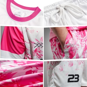 May include: White athletic shirt and shorts set with pink accents. The shirt has a pink collar and sleeve details. The shorts feature a pink and white abstract design and the number 23. The shorts have a drawstring waist.