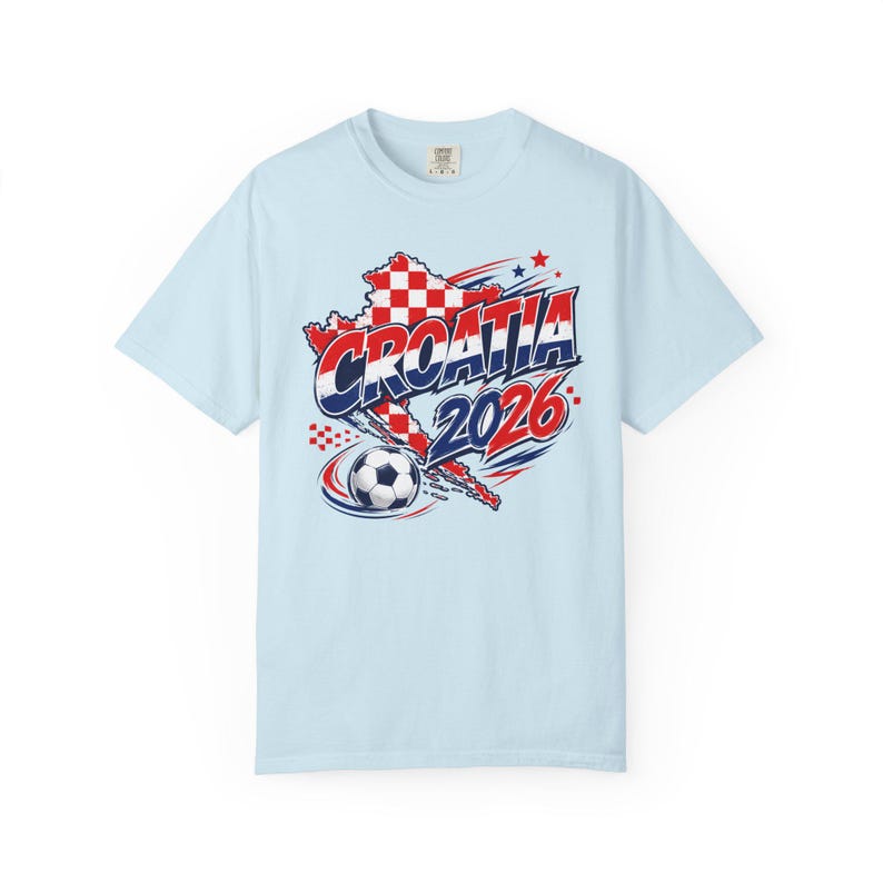 May include: Light blue t-shirt featuring a graphic design related to Croatia. The design includes the word "CROATIA" in red and white, the year "2026", a soccer ball, and a map outline of Croatia in red and white checkered pattern.