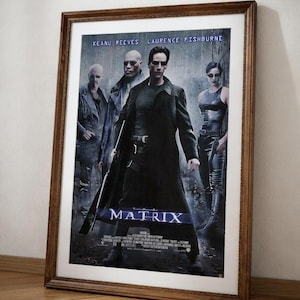 May include: A framed movie poster for "The Matrix" featuring Keanu Reeves and Laurence Fishburne. The poster has a dark color scheme with the title "MATRIX" in large, stylized letters. The poster is in a brown wooden frame.