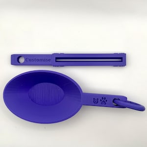 Peut inclure: Une cuillère violette pour aliments pour animaux de compagnie avec une empreinte de patte et un motif de visage de chat. La cuillère a une poignée avec un anneau. Un presse-tube violet assorti avec le mot "Customise" est également montré.